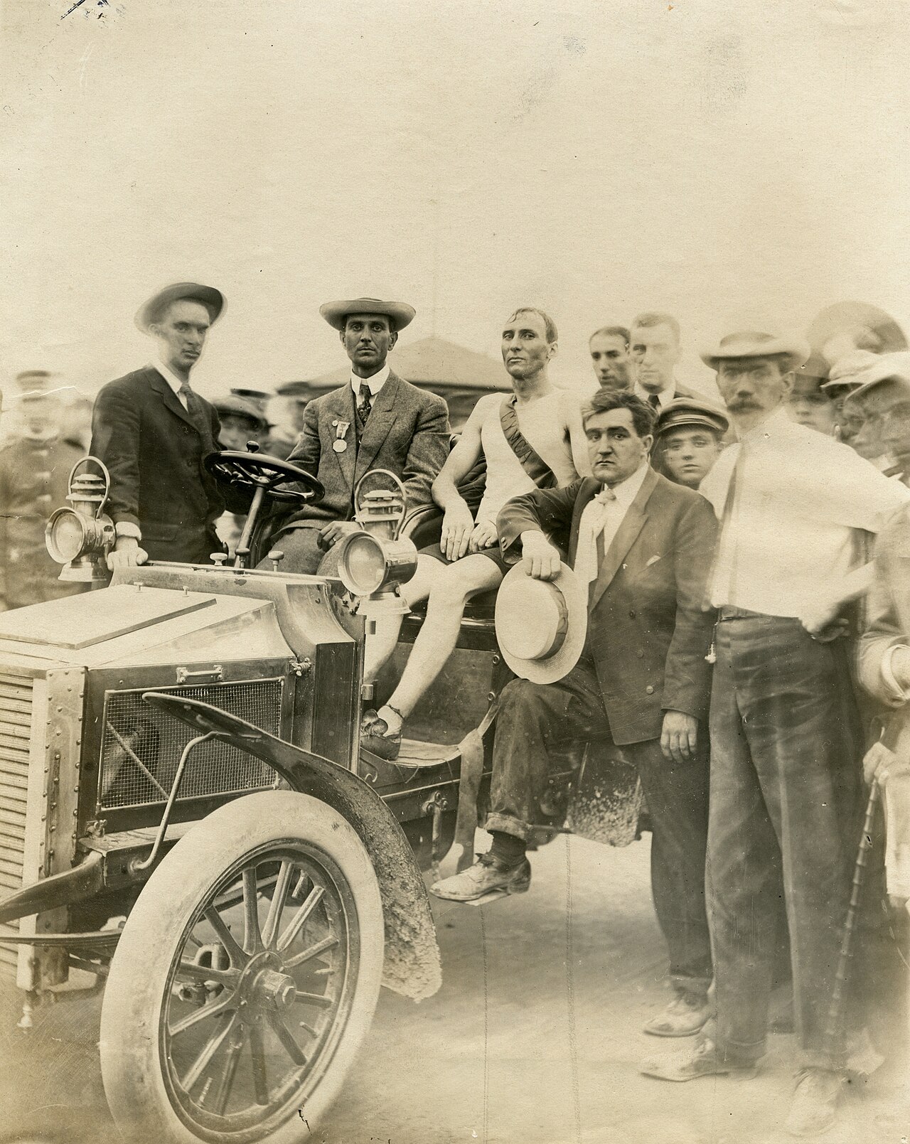 Thomas Hicks sitting in a car after the 1904 marathon, surrounded by onlookers